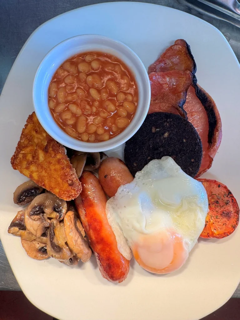 A full breakfast: bacon, sausage, black pudding, fried egg, hash brown, mushrooms, grilled tomato and a pot of beans.